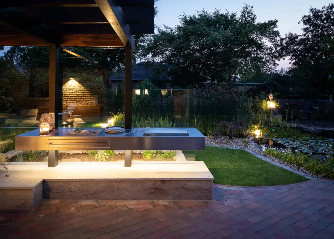 Moderner Grillplatz im Garten mit integrierter Beleuchtung und Teich. Perfekt f&uuml;r laue Sommerabende.