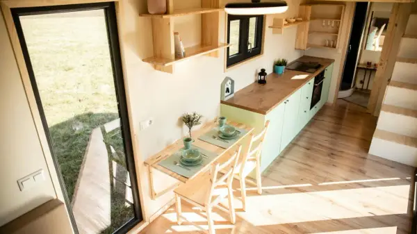 Gemütliches tiny house innen mit Esstisch, Küche und Blick ins Grüne.