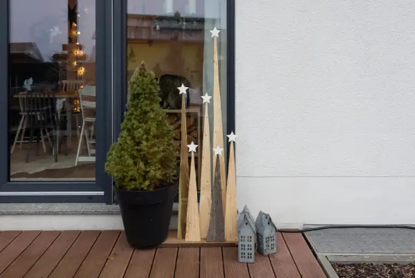 Selbstgemachte Weihnachtsdeko außen: Tannenbaum im Topf, Holz-Tannenbäume mit Sternen und kleine Lichterhäuser auf einer Holzterrasse.