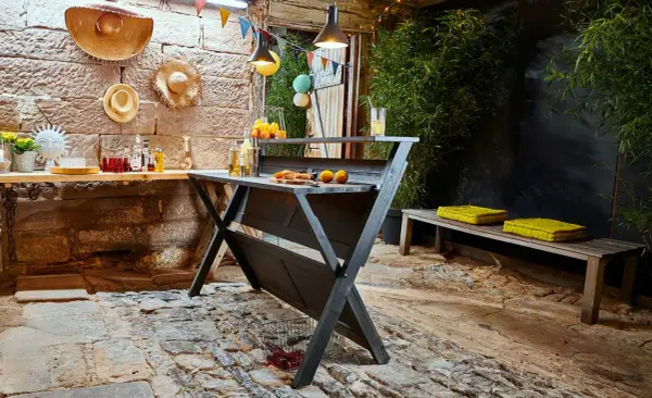 Rustikale Bar selber bauen: Eine dunkle Holzbar mit Orangen und Getränken, dekoriert mit bunten Wimpeln und Hüten. Perfekt für Gartenpartys.